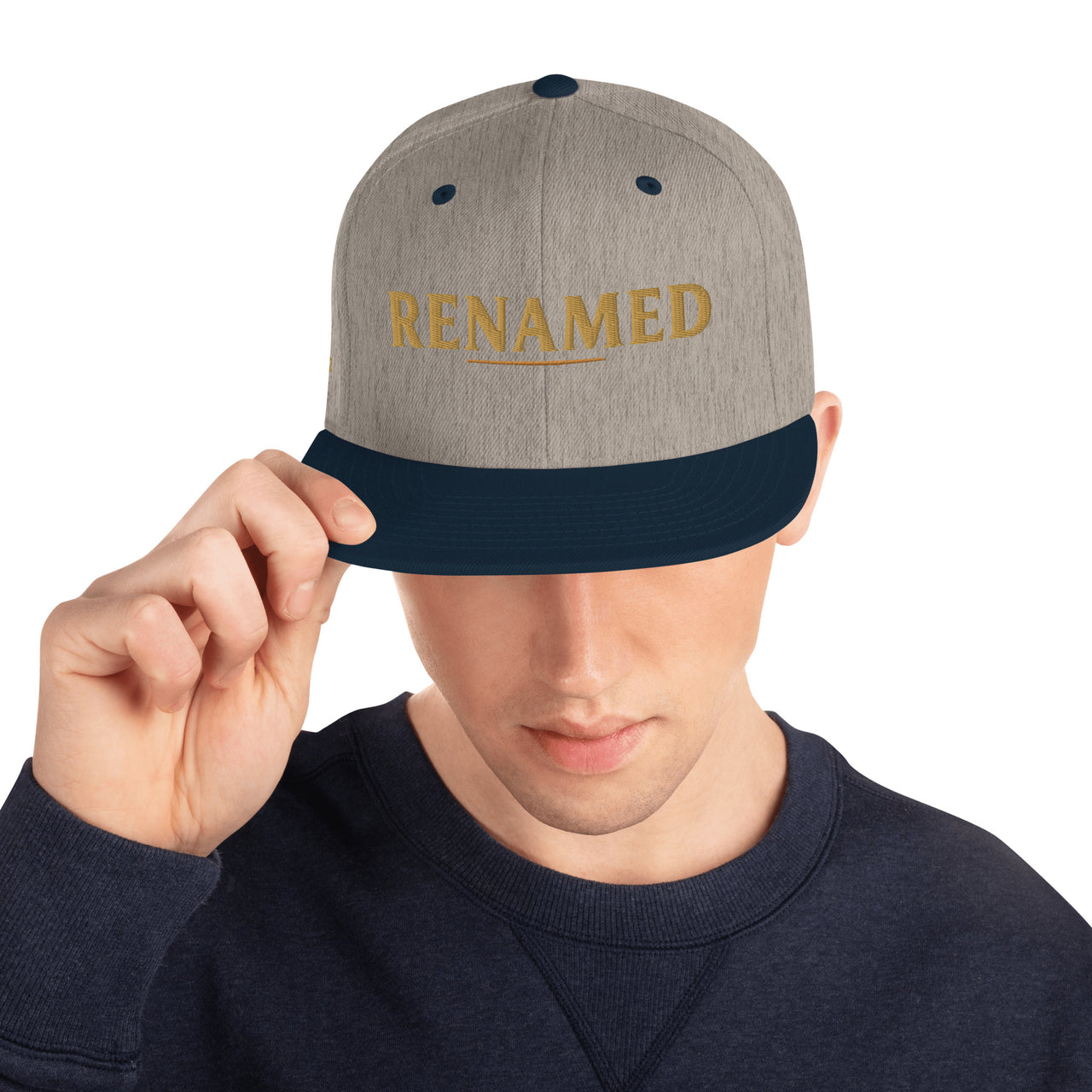 Male model wearing Renamed Classic Snapback in Heather Grey/Navy, front view with “RENAMED” embroidered in Old Gold