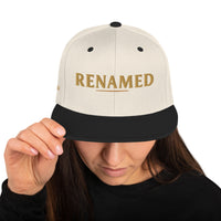 Female model wearing Renamed Classic Snapback in Natural/Black, front view with “RENAMED” embroidered in Old Gold