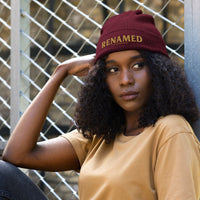 Female model wearing Renamed Organic Ribbed Beanie in Burgundy, front view with Old Gold embroidery