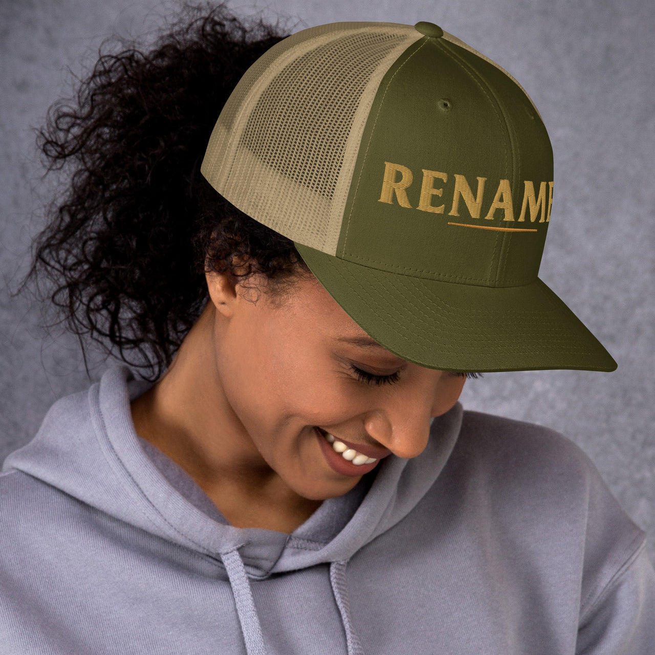 Female model wearing Renamed Trucker Cap in Moss/Khaki, front embroidery close-up (right front position)