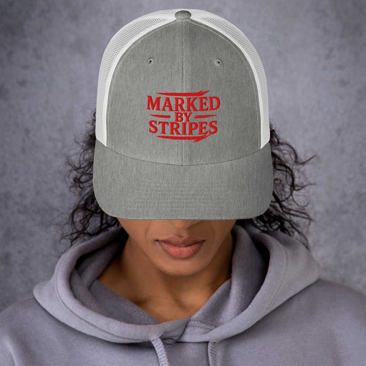 Woman wearing heather grey and white Christian trucker hat – red Marked by Stripes embroidery front view