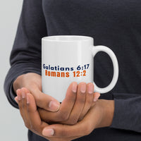 Model holding 11oz Christian mug – scripture side featuring Romans 12:2 and Galatians 6:17