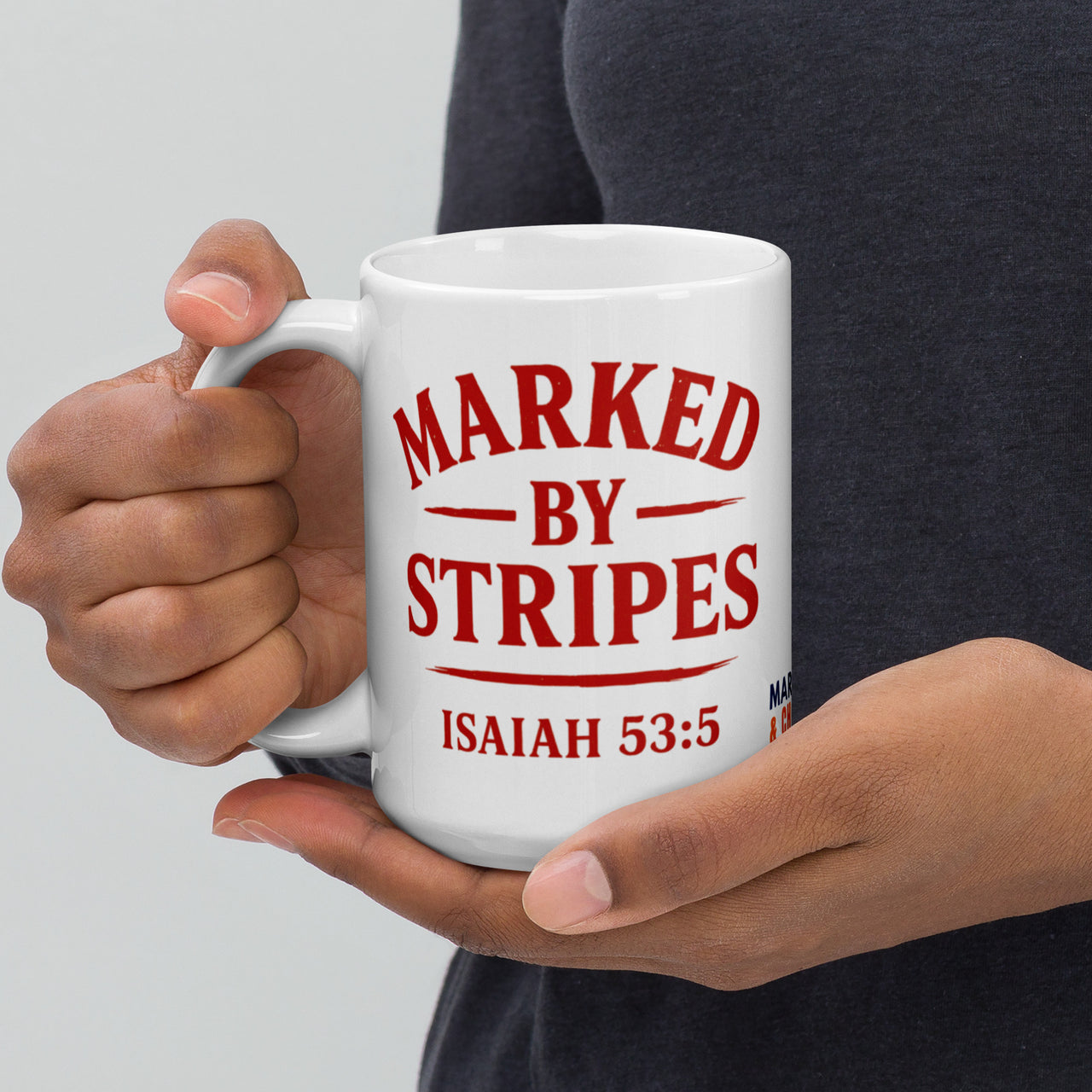 Model holding 15oz Marked by Stripes glossy ceramic mug – red embroidered logo side visible